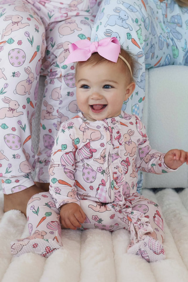 baby girl sitting on floor in pink easter ruffle zipper footie with matching pajama pants in the background 