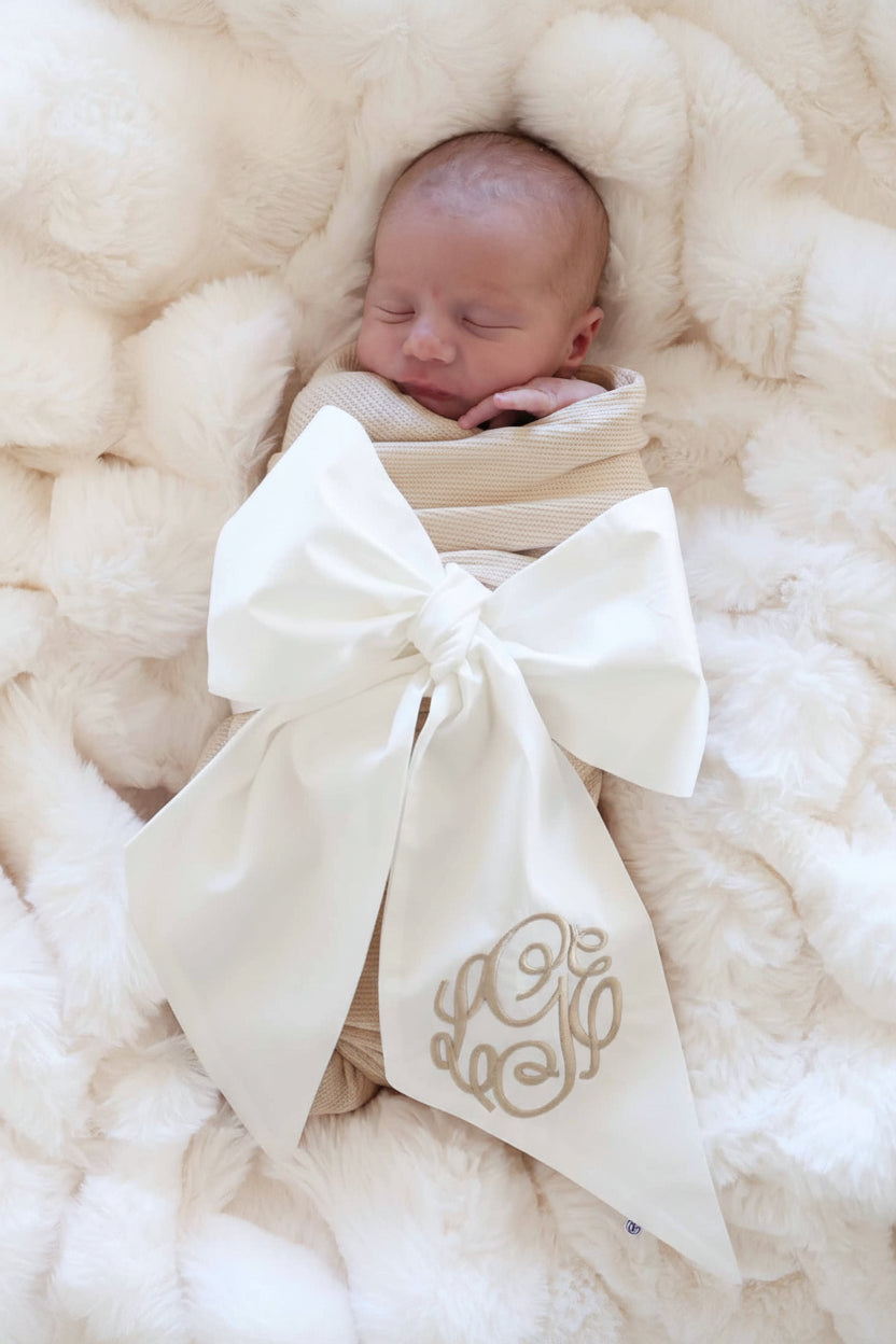 baby wrapped in ivory sash with neutral embroidered monogram 