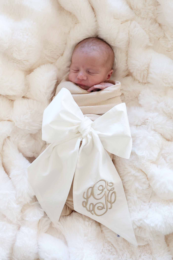 baby wrapped in ivory sash with neutral embroidered monogram 
