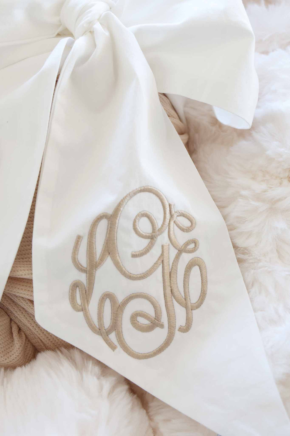 closeup of ivory bow sash with neutral script monogram for babies 