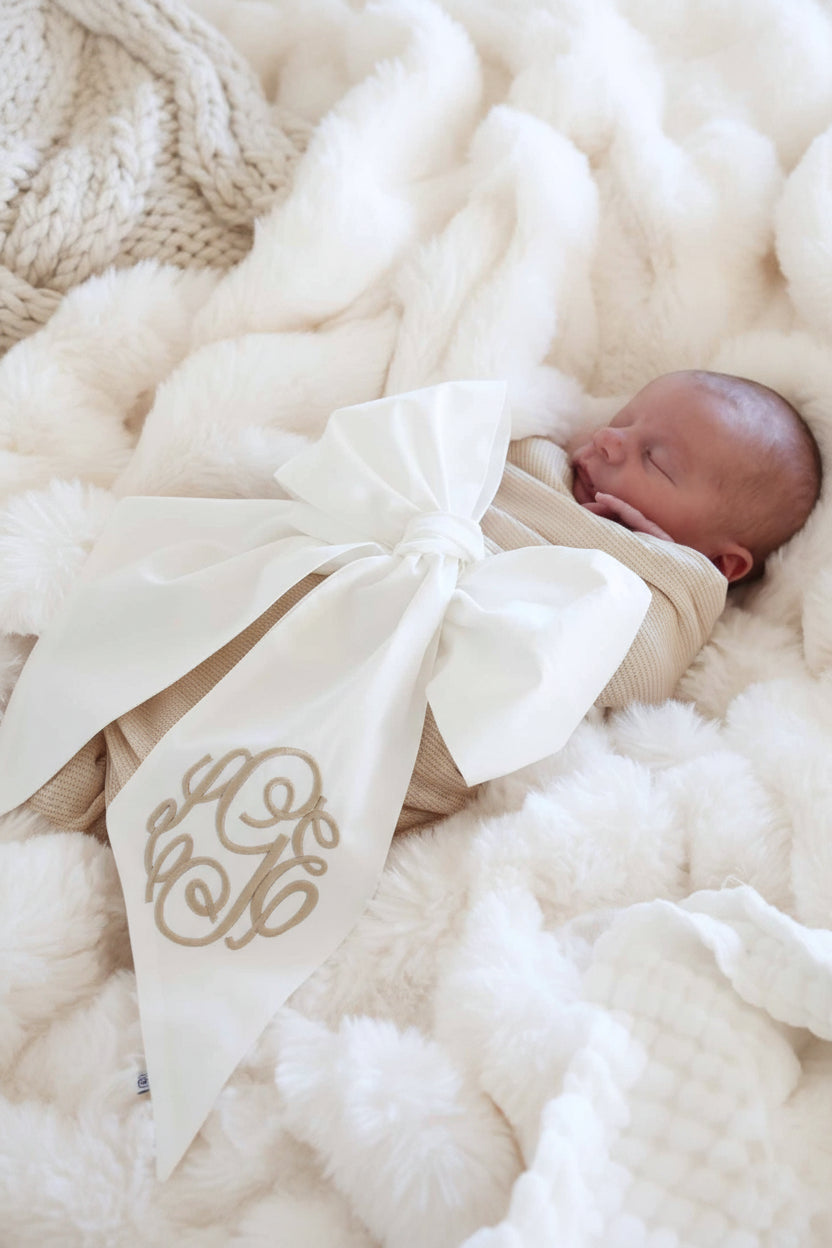 baby wrapped in ivory bow sash with neutral embroidered monogram for newborn pictures 