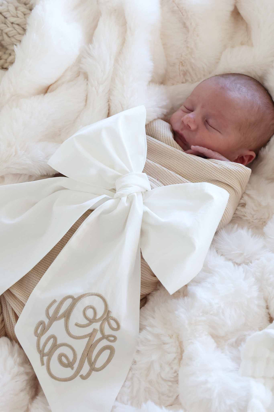 newborn baby wrapped up in ivory bow with embroidered monogram in script font 