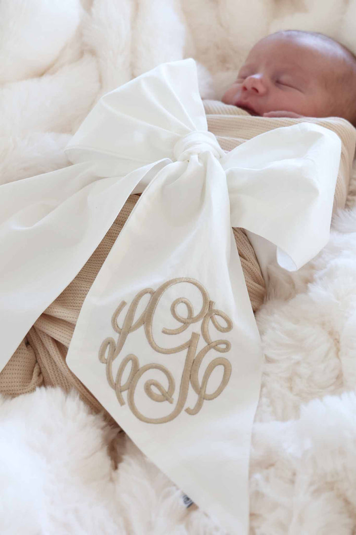 newborn baby wrapped up in ivory bow with embroidered monogram in script font 