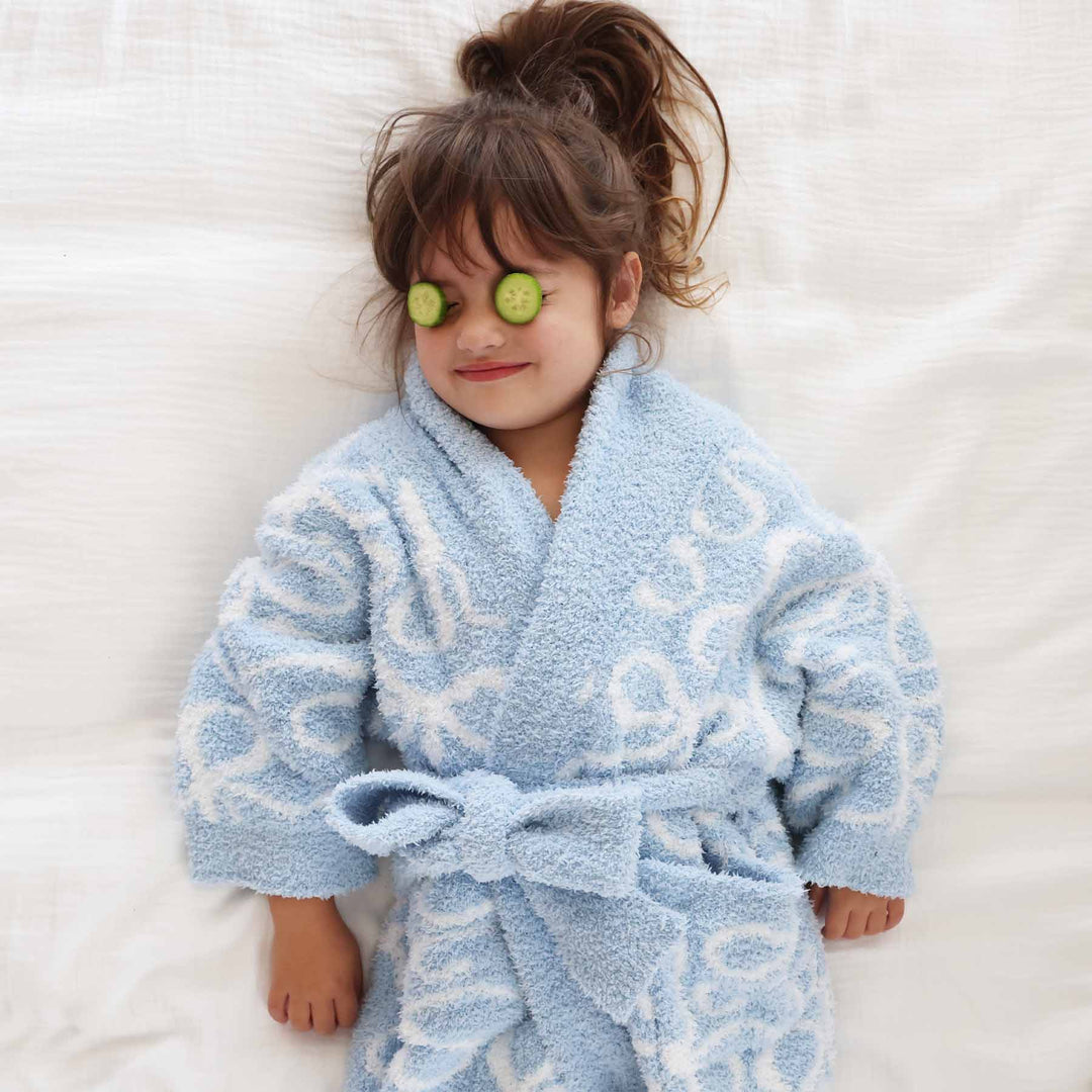 girl laying on a bed in a blue and white bow long sleeve plush robe with cucumbers on her eyes 