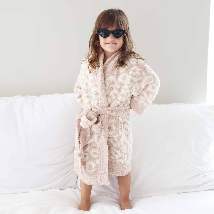 girl standing on a bed with her hands on her hips with black point sunglasses wearing a neutral leopard robe that ties at the waist 