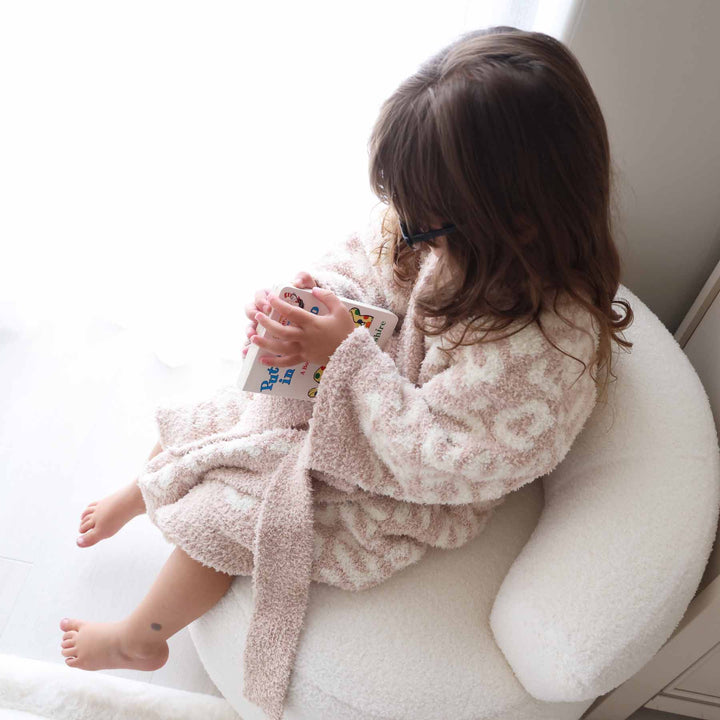 girl sitting on a chair wearing a tan leopard plush robe reading a book 