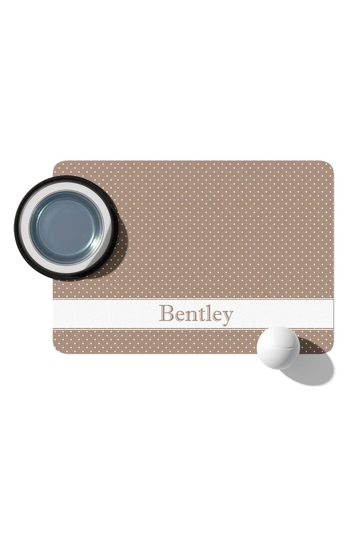 Personalized latte brown polka dot pet placemat with a pet food bowl on top and the name 'Bentley' in a white banner