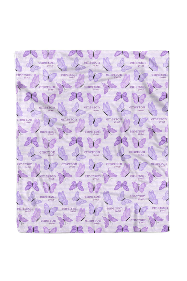 Flat lay of a fully unfolded personalized Caden Lane Lavender Wings blanket in lavender striped fabric, showing the full repeating pattern of purple butterflies and custom name