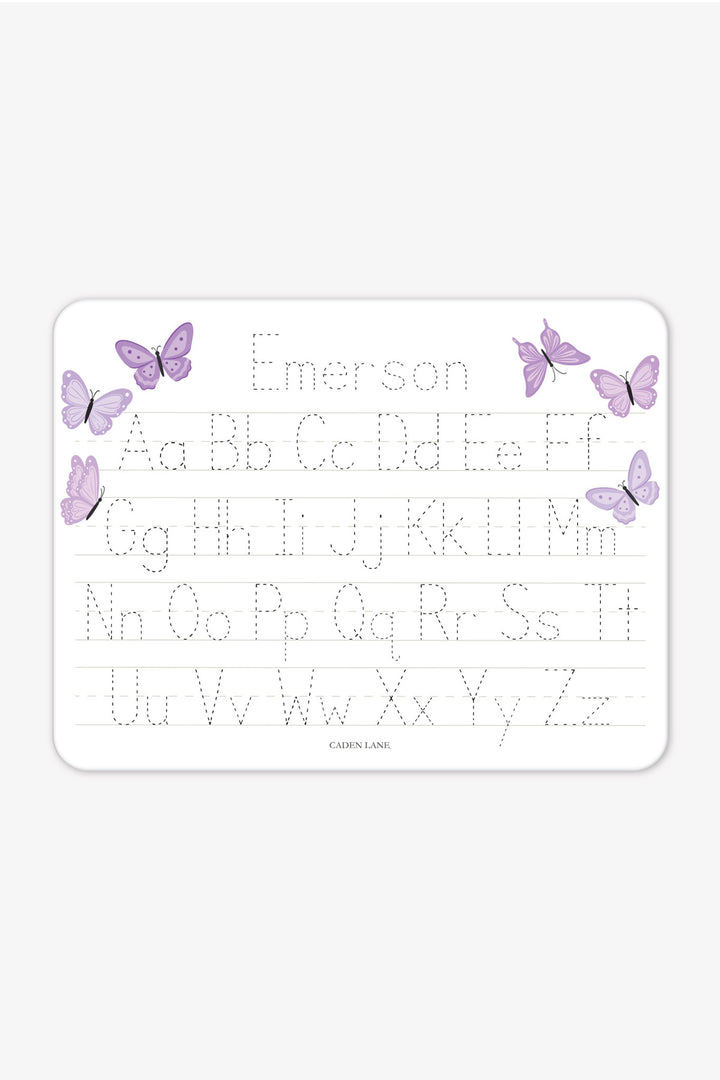 Flat lay of a personalized Caden Lane Lavender Wings alphabet whiteboard, showing purple butterflies and tracing letters with custom name