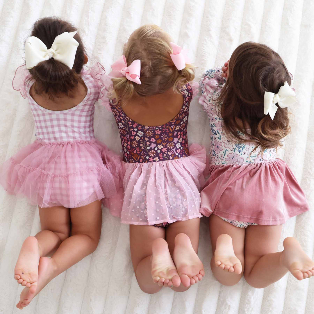 three girls wearing floral and gingham leotards laying on stomach on the floor