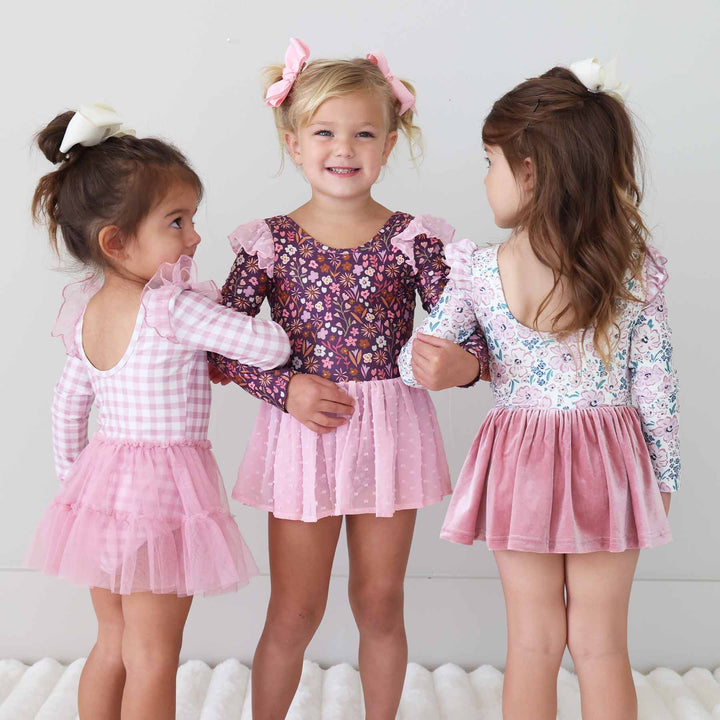 three girls with interlocking arms wearing long sleeve fall toned leotards 