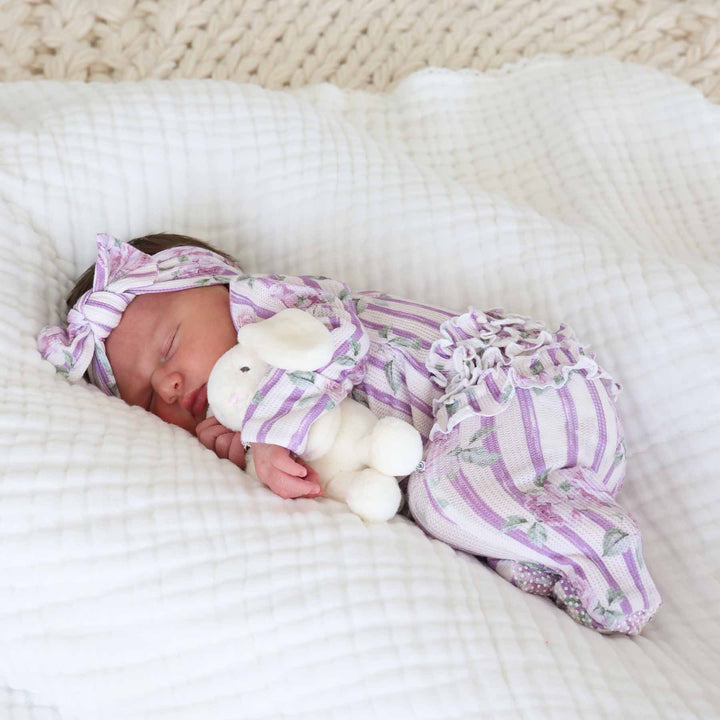 baby holding tiny bunny stuffed animal in lila's lilacs ruffle zipper footie and matching headwrap