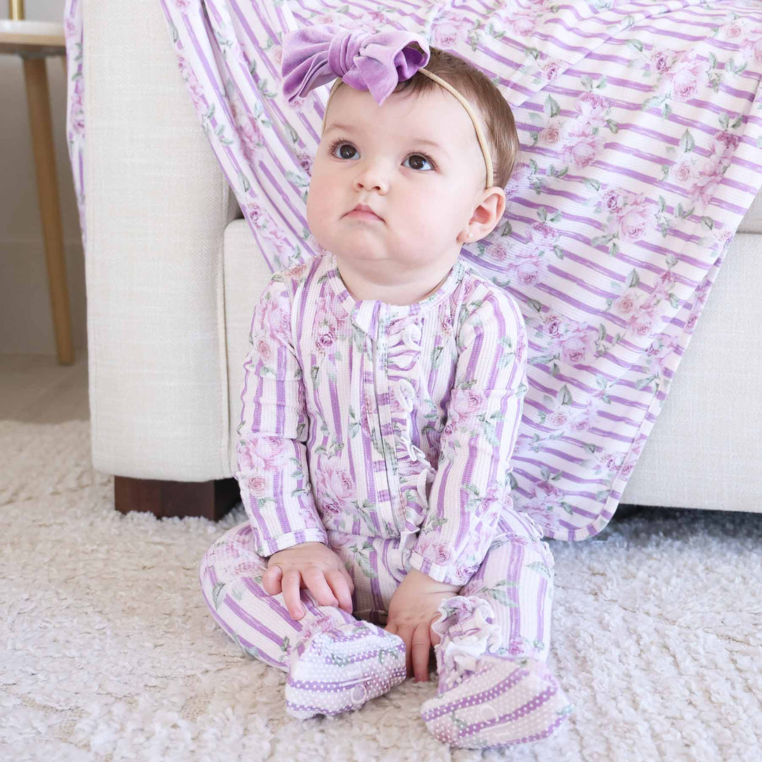 sitting baby wearing lila's lilacs footie with ruffle along the zipper with purple velvet bow headband 