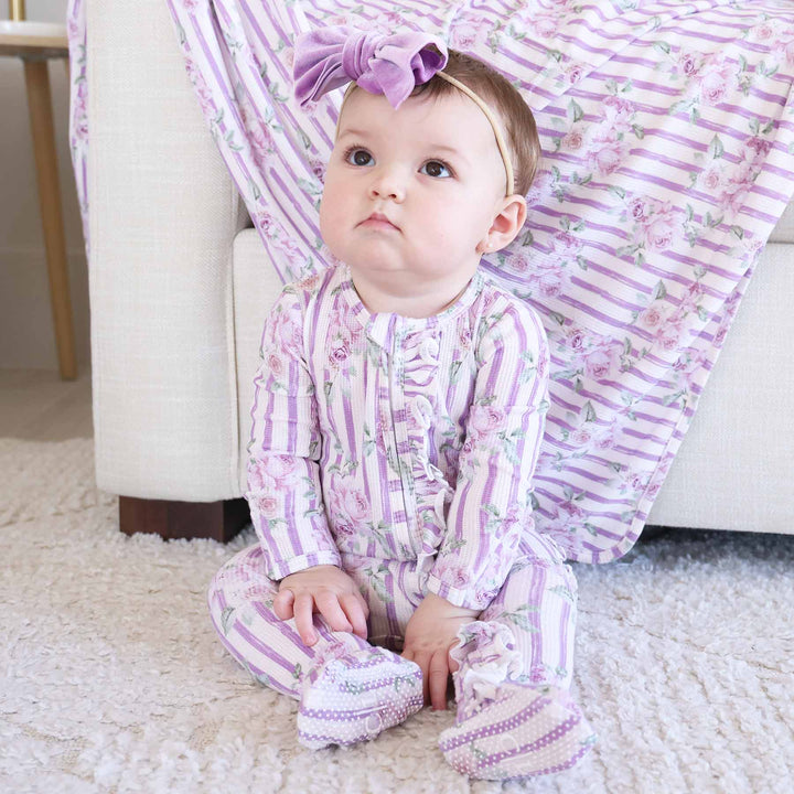 sitting baby wearing lila's lilacs footie with ruffle along the zipper with purple velvet bow headband 