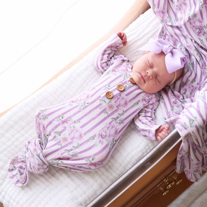 baby laying in bassinet wearing lila's lilacs newborn knot gown and hat set with purple ribbon bow and matching swaddle 