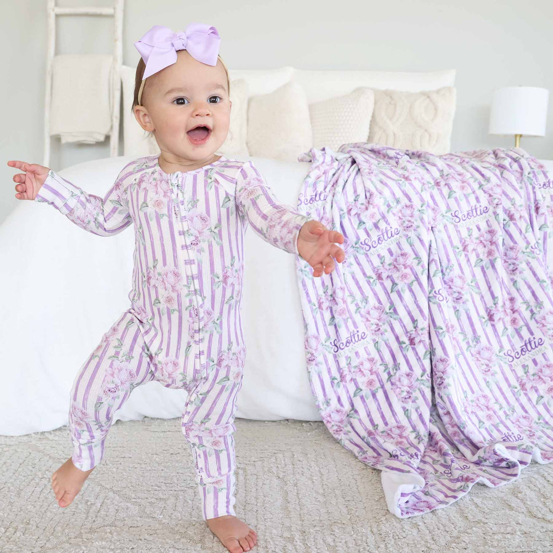 baby girl wearing purple stripe and rose bamboo waffle convertible zip romper with flip mitts and footies with matching blanket in the background 