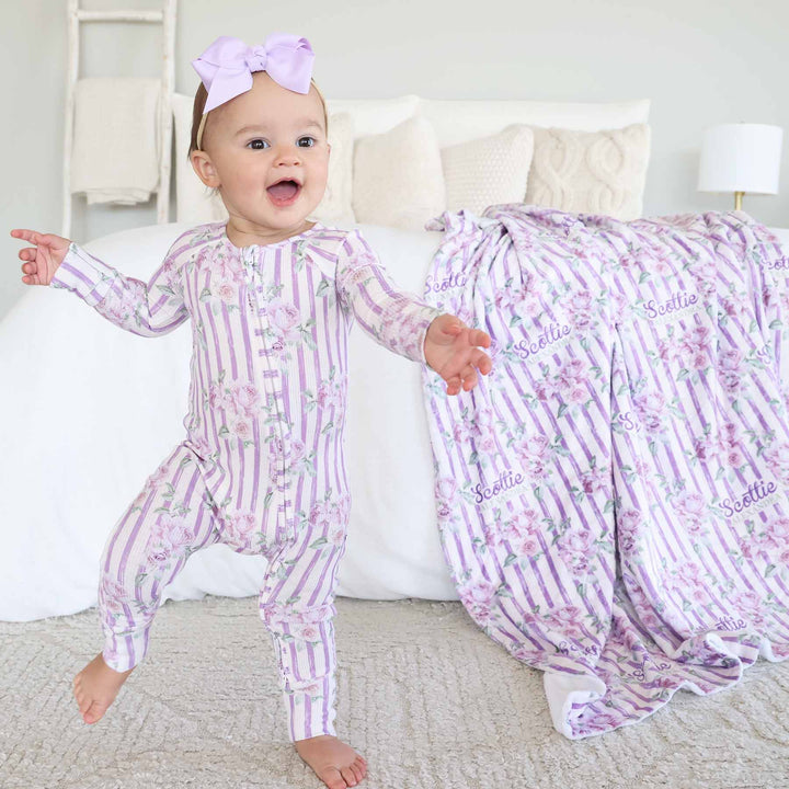 baby girl wearing purple stripe and rose bamboo waffle convertible zip romper with flip mitts and footies with matching blanket in the background 
