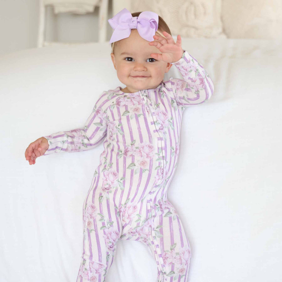 standing baby girl wearing lila's lilacs bamboo waffle convertible zip romper with matching lila's lilacs ribbon bow headband