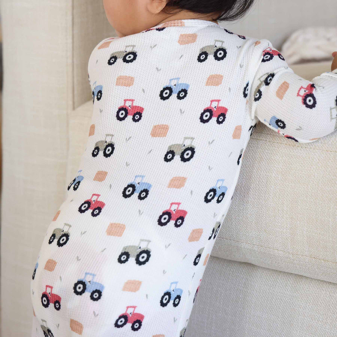 baby boy leaning against a couch wearing tractor and hay bale footie pajama 