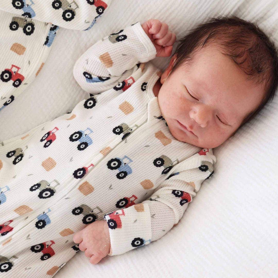 red, green and blue tractor bamboo waffle zipper footie with hay bales and grass sprigs