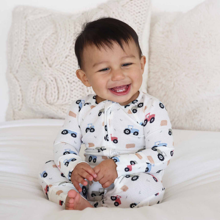 toddler boy sitting on bed wearing tractor zip romper pajama 