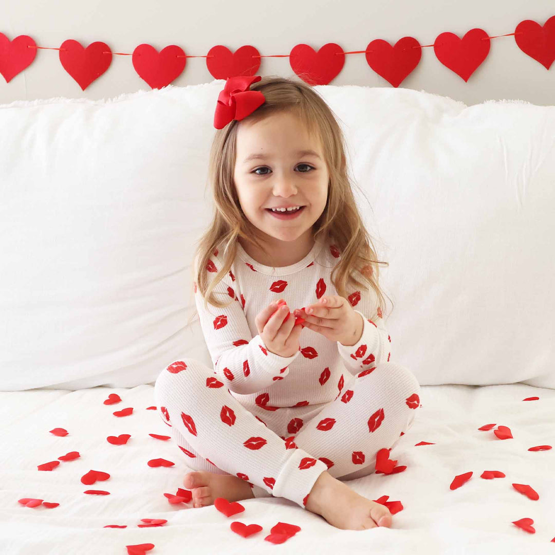 girl sitting on bed in red kiss two piece pajama set for kids 