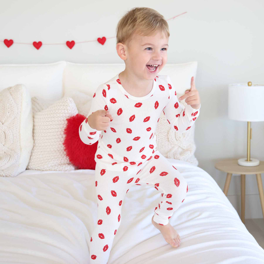 boy jumping on the bed in little kisses two piece pajama set for kids gender neutral