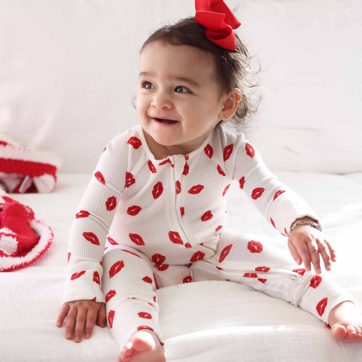 baby girl wearing a convertible zip romper pajama for valentine's day with red lips on it and flip mitts and footies 