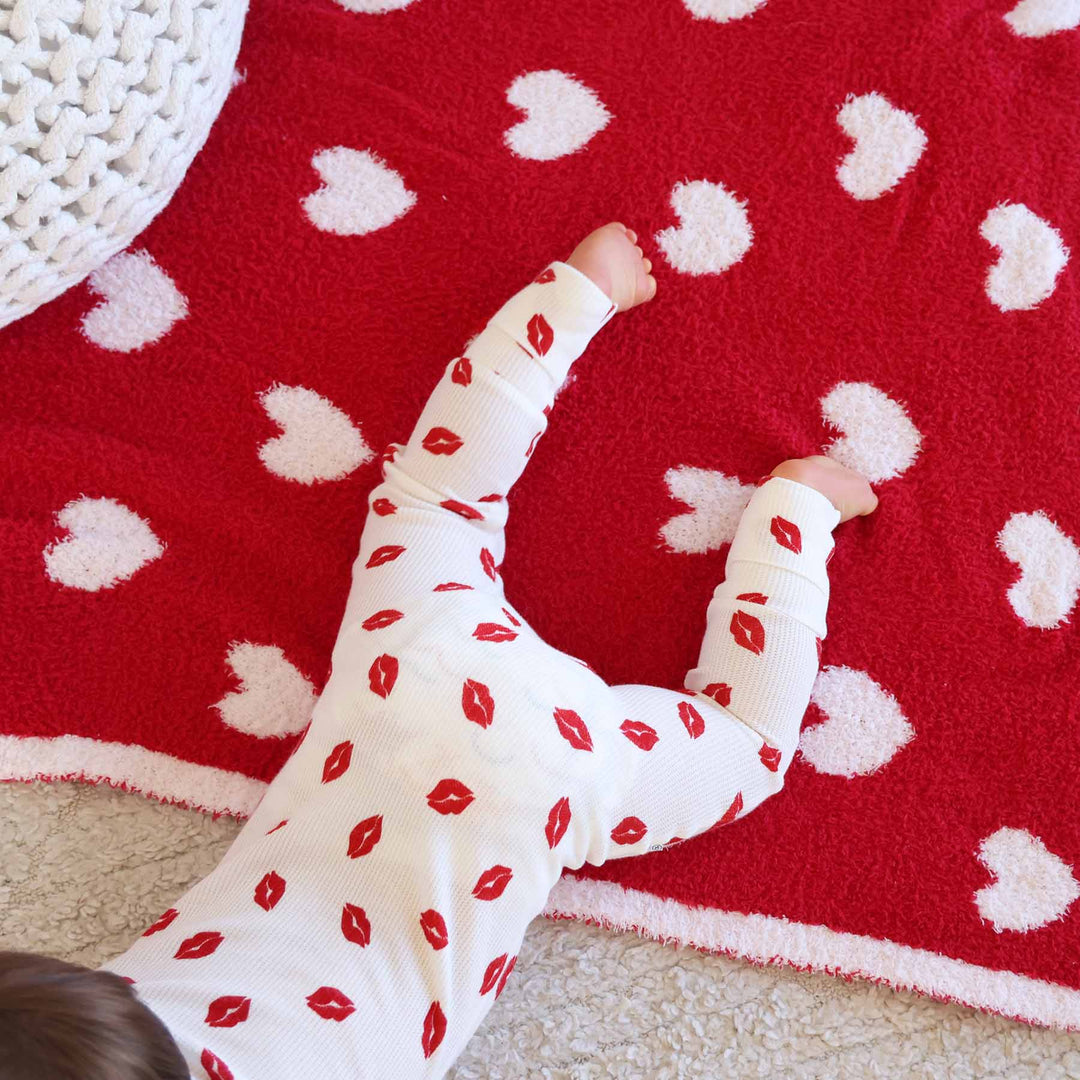 baby laying on stomach in red kiss zip romper pajama with a red heart plush blanket underneath