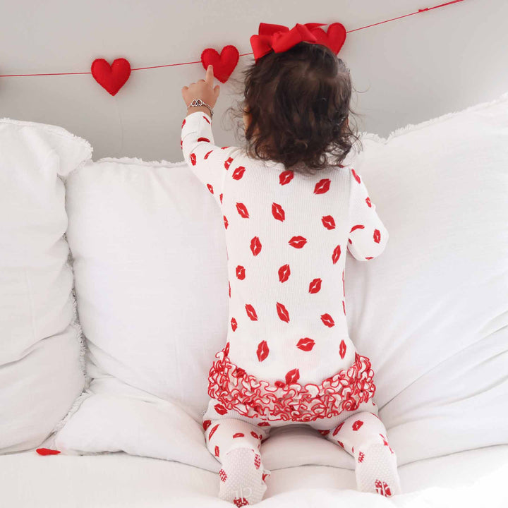 baby girl kneeling wearing a lipstick kiss white and red kiss ruffle zipper footie