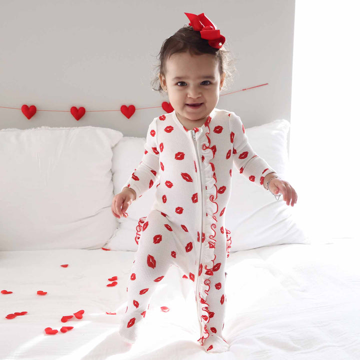 walking baby girl in little kisses zipper footie with ruffle along the zipper 