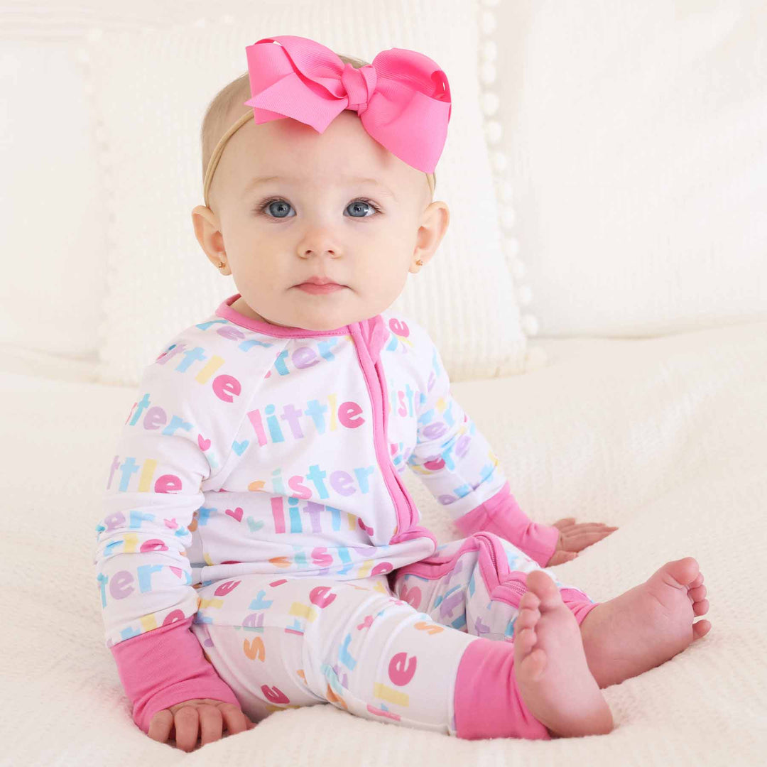 baby girl wearing little sister zip romper and pink bow headband