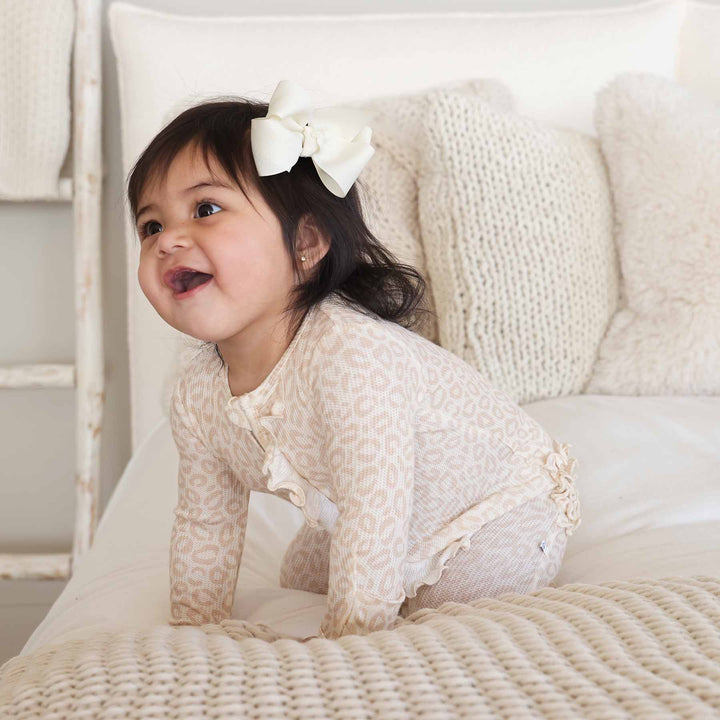 baby girl kneeling and wearing a neutral leopard bamboo viscose footie pajama 