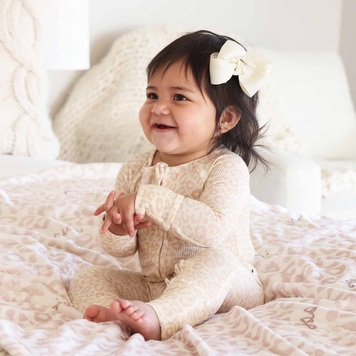 toddler sitting on bed in neutral leopard pajama romper 