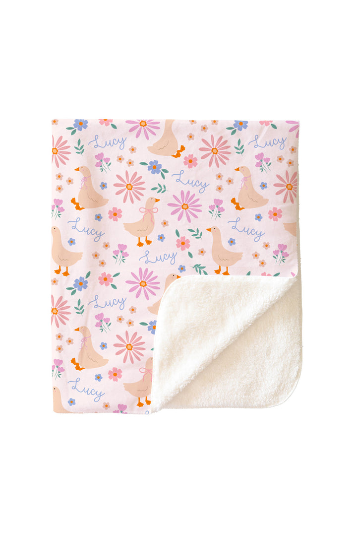 Personalized Kids Blanket sherpa variant in the Lucy Goosy duck and floral print, showing the printed exterior with name Lucy and white sherpa interior revealed at corner