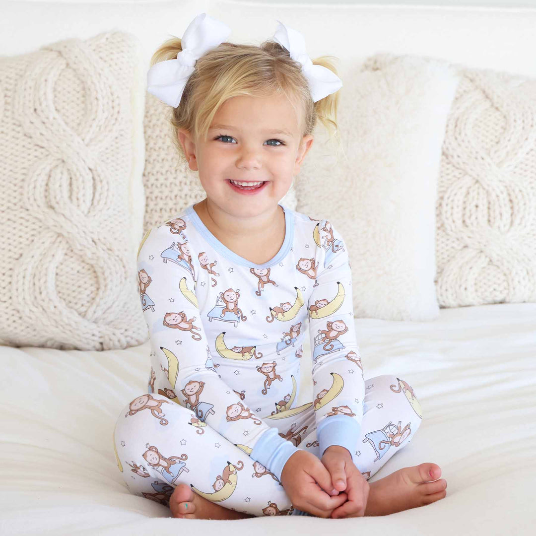 girl sitting on bed wearing monkey and banana pajama set 