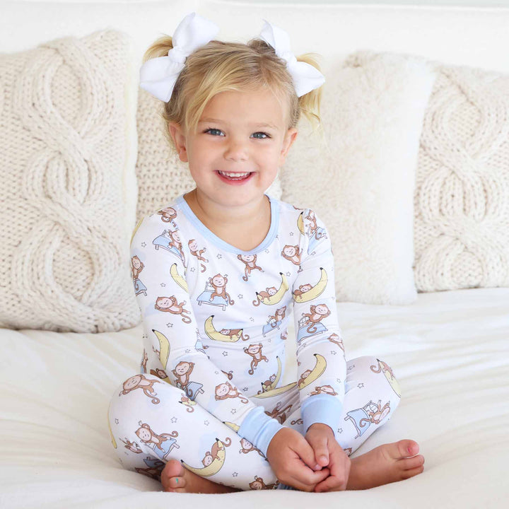 girl sitting on bed wearing monkey and banana pajama set 