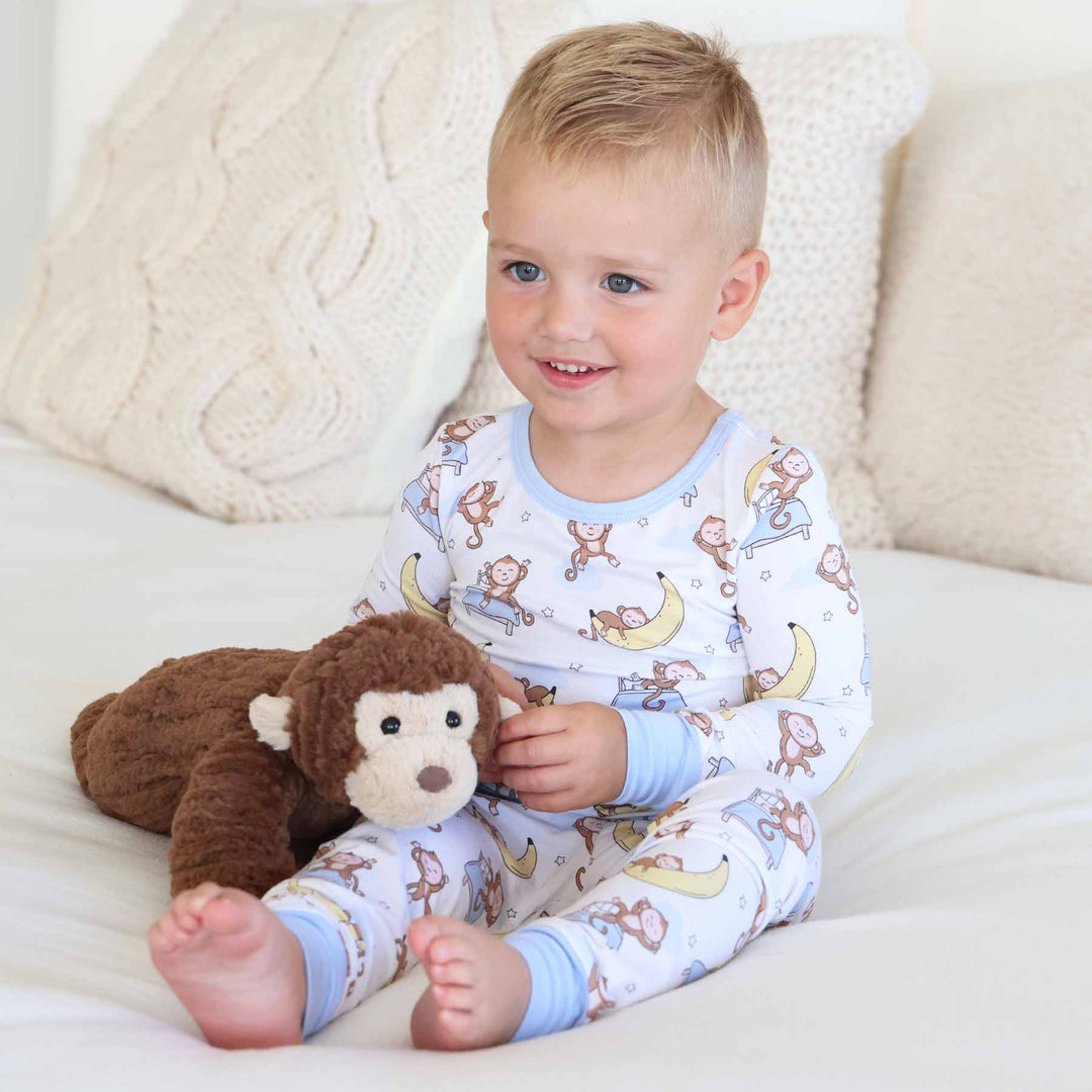 little boy sitting on bed in monkey and banana two piece pajama set 