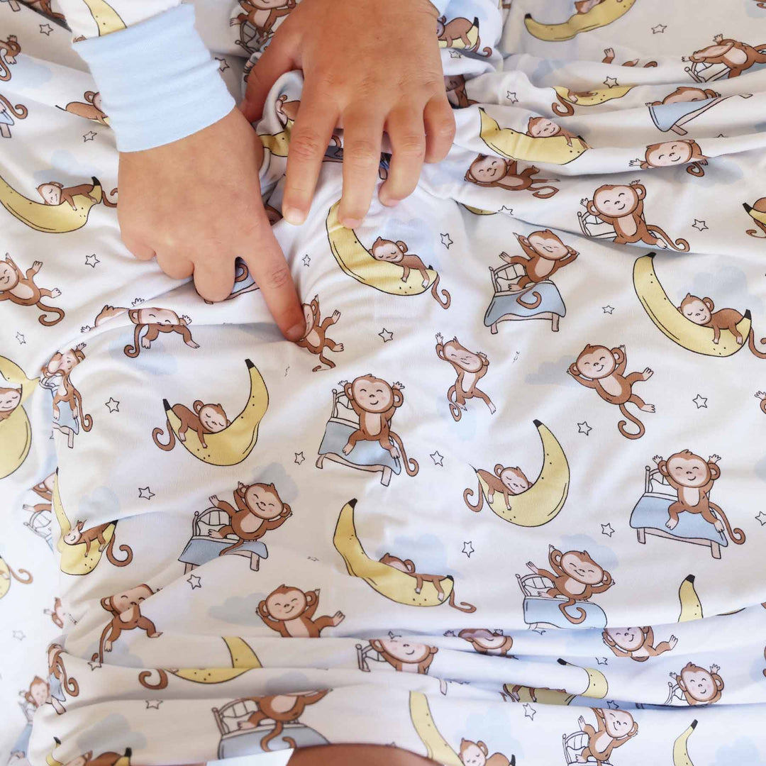 white double sided bamboo blanket with monkeys sitting on beds and sleeping on banana moons with star details 