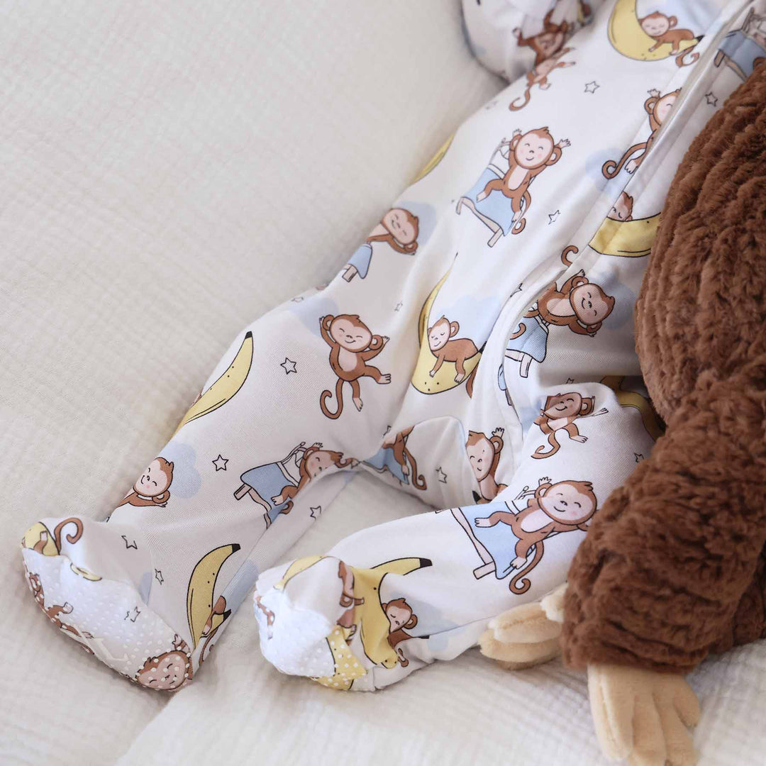 close up of baby laying on bed in money and banana footie next to a monkey stuffed animal 