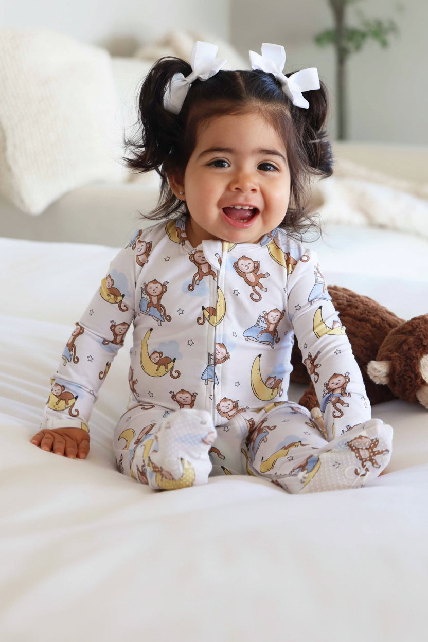 girl sitting on a bed with a monkey and banana moon double sided zipper footie for babies 