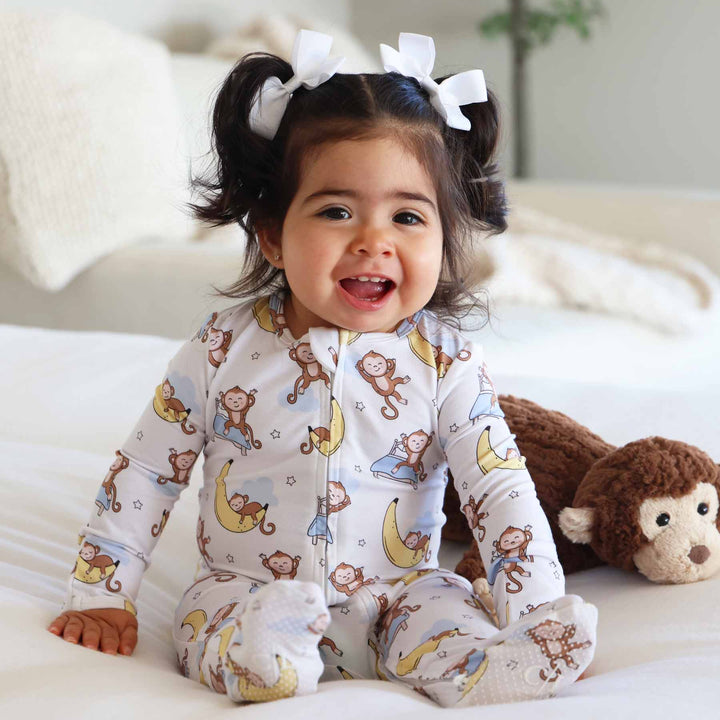 girl sitting on a bed with a monkey and banana moon double sided zipper footie for babies 