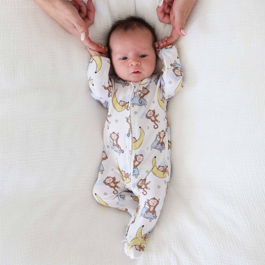 baby laying on bed wearing monkey see, monkey snooze bamboo viscose zipper footie for babies gender neutral