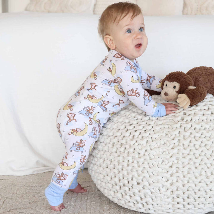 baby wearing monkey and banana convertible zip romper leaning on ottoman with a monkey stuffed animal