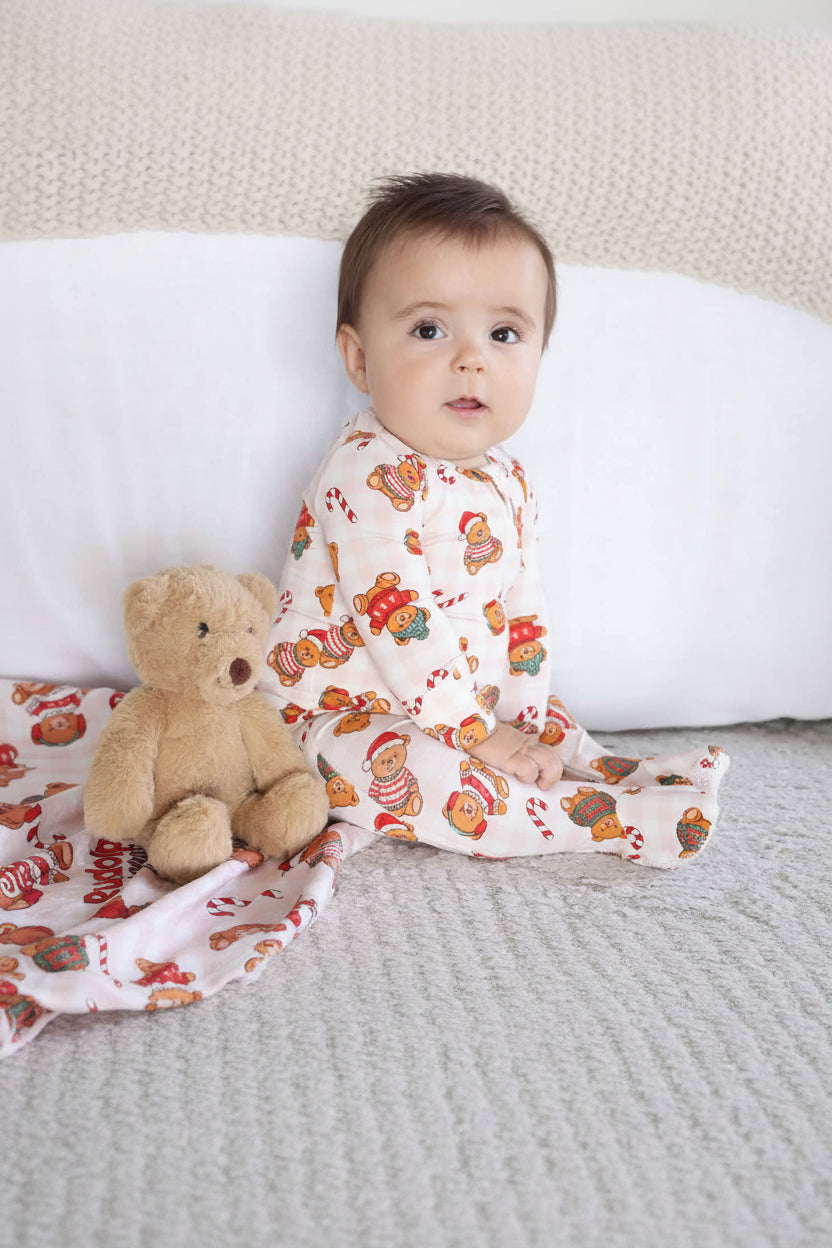 baby boy wearing teddy bear zipper footie for christmas sitting next to a teddy bear stuffed animal 