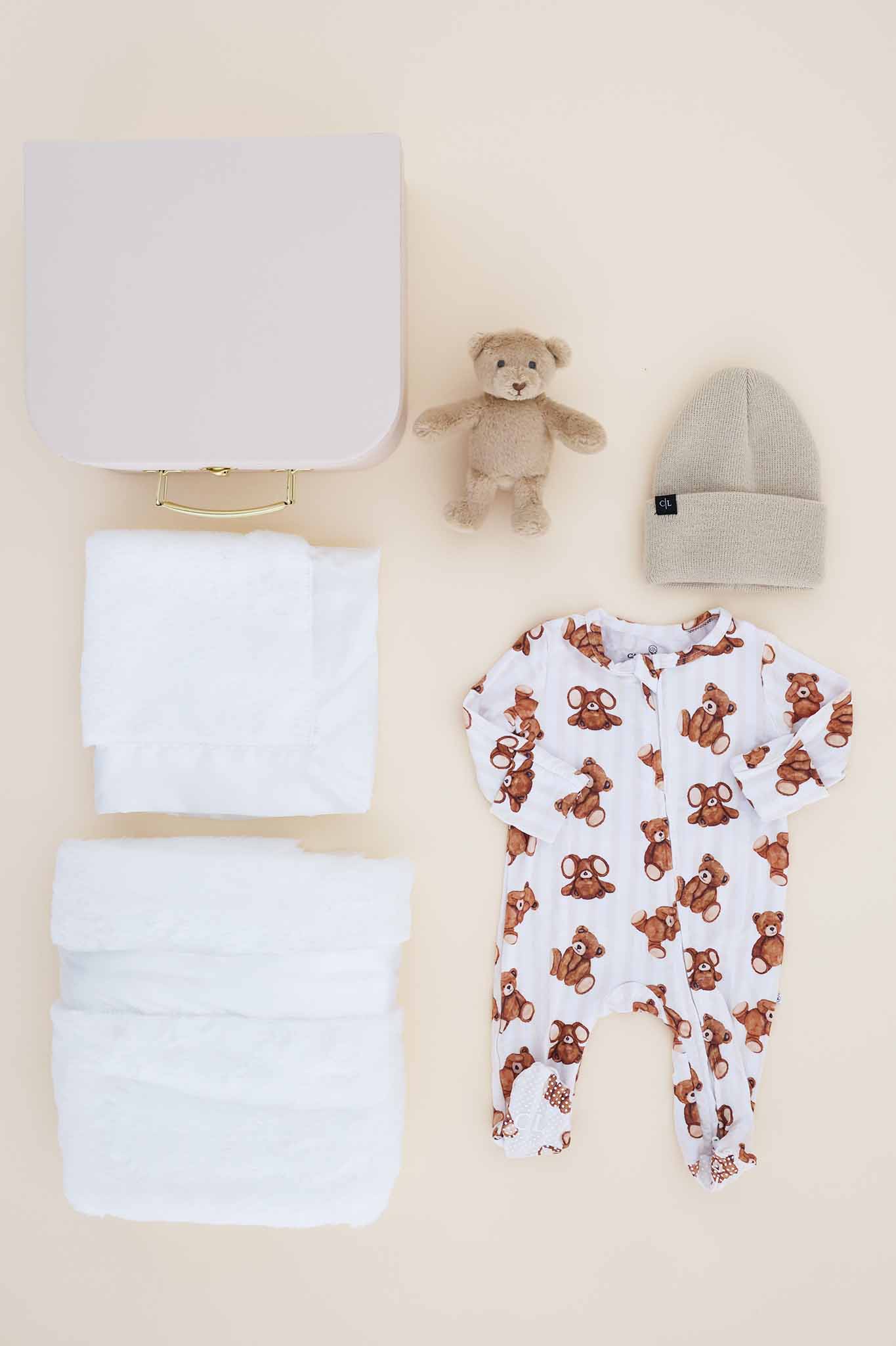 contents of gender neutral newborn keepsake box with bear footie, white blanket, lovey, beanie and stuffed bear