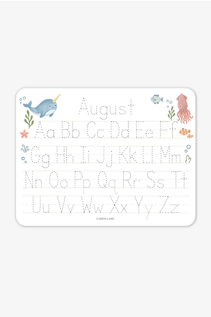 Flat lay of a personalized Caden Lane Ocean Dreams alphabet whiteboard, showing narwhal, fish, and squid with tracing letters and custom name