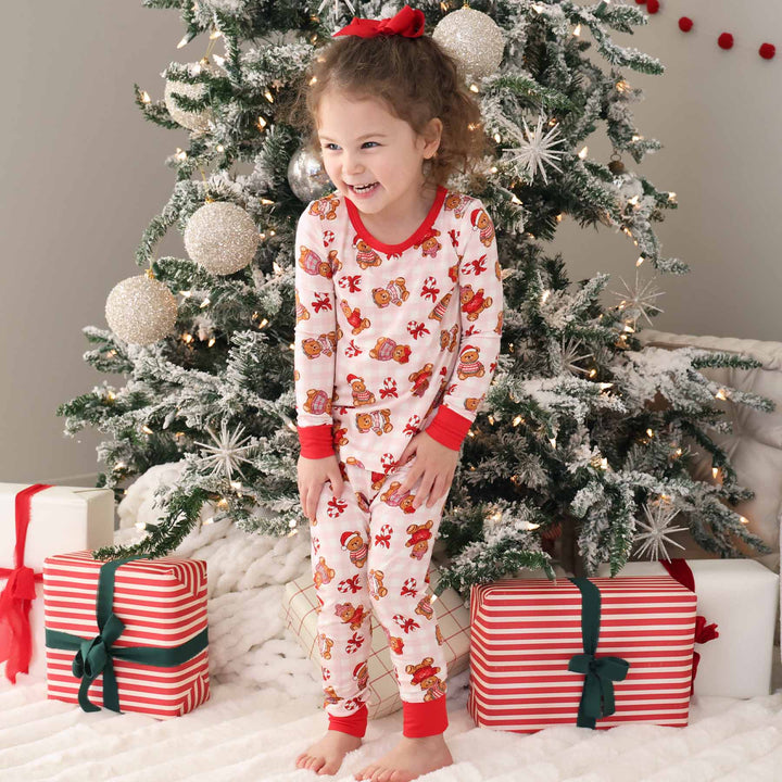 girl wearing pink beary christmas two piece pajama set standing in front of a christmas tree with presents 