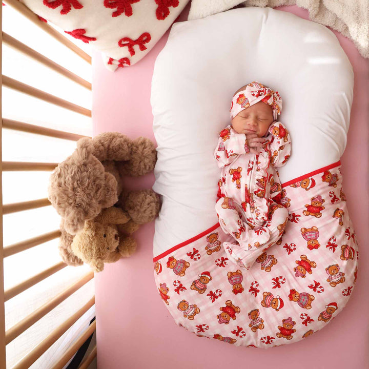 baby in pink gingham christmas teddy bear ruffle footie laying in crib  