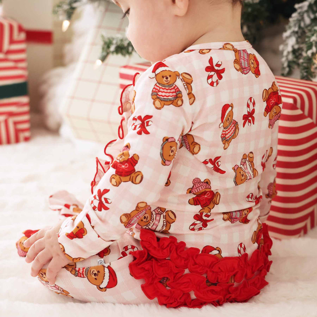 baby sitting under the christmas tree in a ruffle bottom zipper footie with a pink gingham, christmas sweater teddy bear and candy cane print